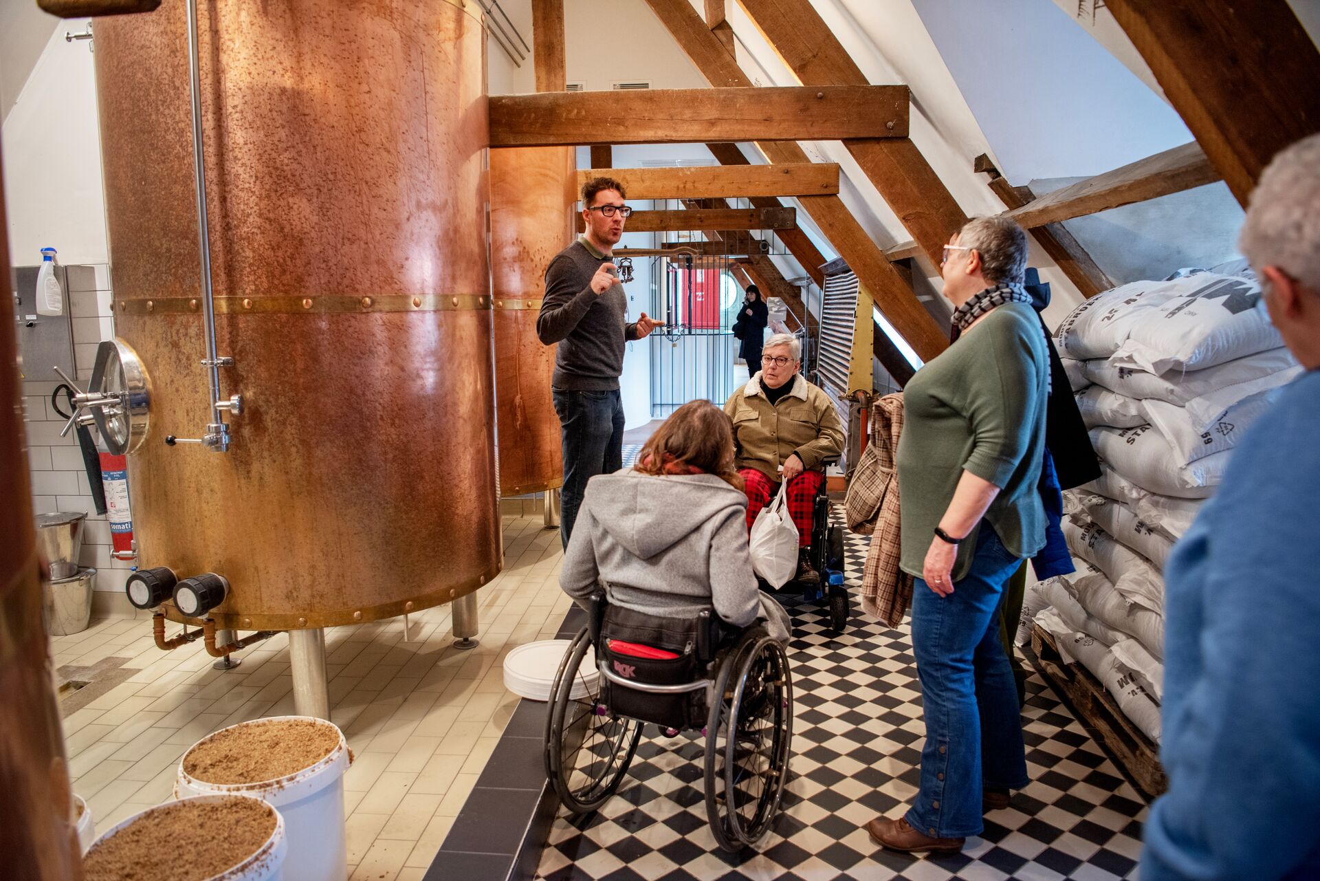 Brewery tour at Bourgogne des Flandres Brewery tour: guide talks by a copper kettle, visitors listen beside sacks of malt.