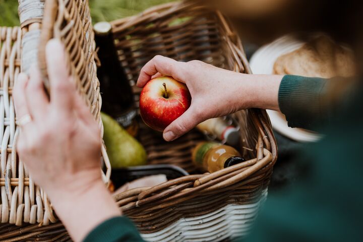 Een vrouw legt een appel in een gevulde picknickmand.