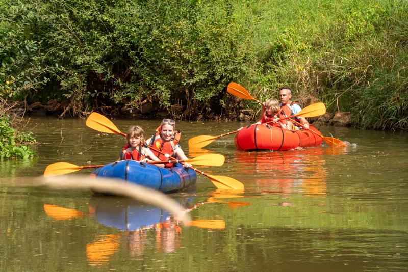 Deux kayaks gonflables avec des pagayeurs sur une rivière calme, entourée de verdure.