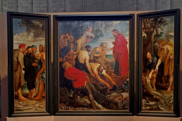 "Een groot drieluik schilderij toont bijbelse scènes met meerdere figuren in vloeiende gewaden. Het centrale paneel toont een dramatische zee-interactie, met personen die een visnet binnenhalen, hun gezichten intens en geconcentreerd. Links en rechts zijn