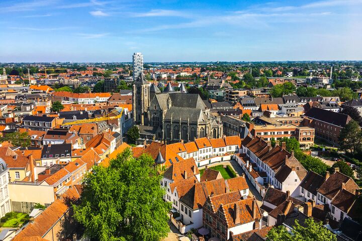 Kortrijk from Above: Historic Charm and Gothic Heritage Aerial view of a European city with red-tiled roofs and a prominent Gothic cathedral, surrounded by trees under a clear blue sky, conveying historic charm.