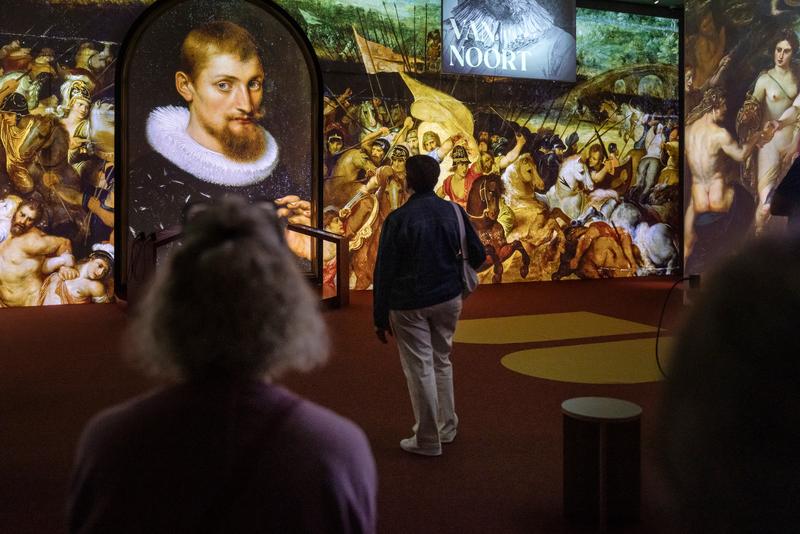 Een persoon staat in een museum en bekijkt een levendige digitale presentatie van klassieke kunst. De gedetailleerde scène creëert een meeslepende en contemplatieve sfeer.