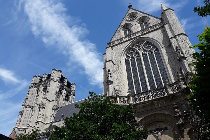 Sint-Jacobskerk A towering Gothic cathedral façade and bell tower against a bright blue sky, adorned with ornate stone details and large arched windows, creating a majestic atmosphere.