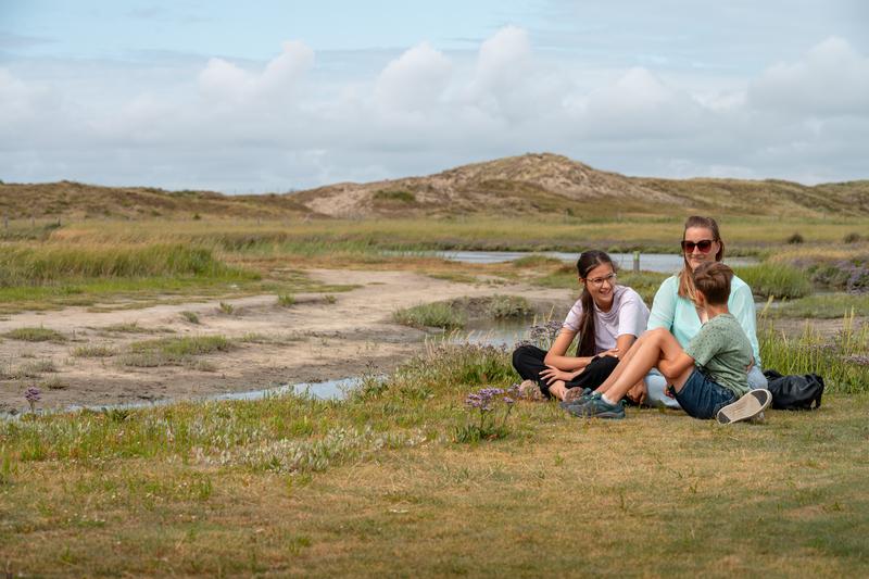 Een familie van 3 zit tussen de duinen in de Zwinstreek.