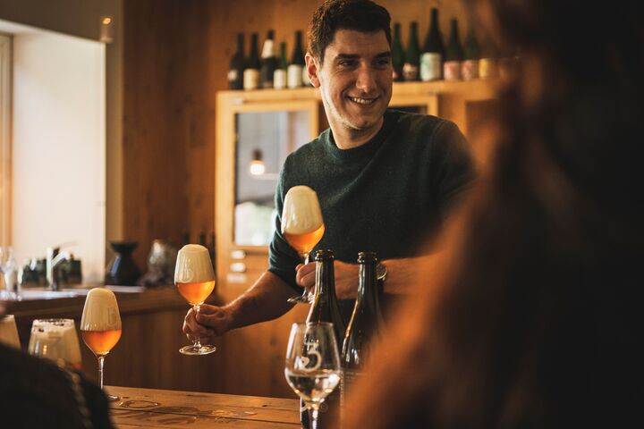 Een man staat achter een toog terwijl hij gevulde glazen bier vasthoudt.