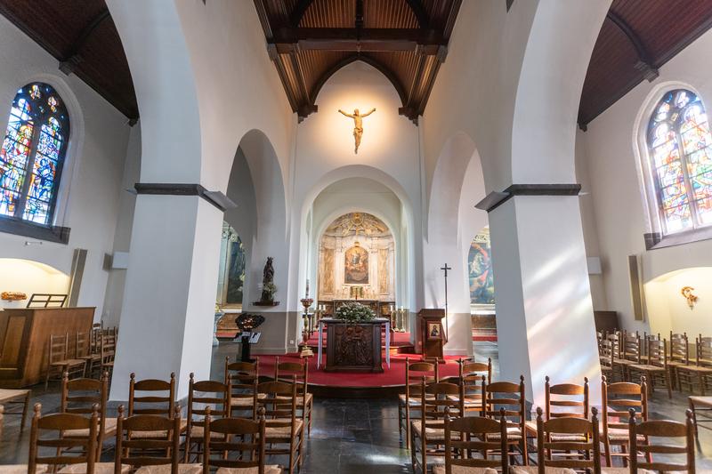 Interior de una iglesia con altos arcos, techo de madera y vidrieras. Un crucifijo está montado sobre el altar, creando una atmósfera serena.
