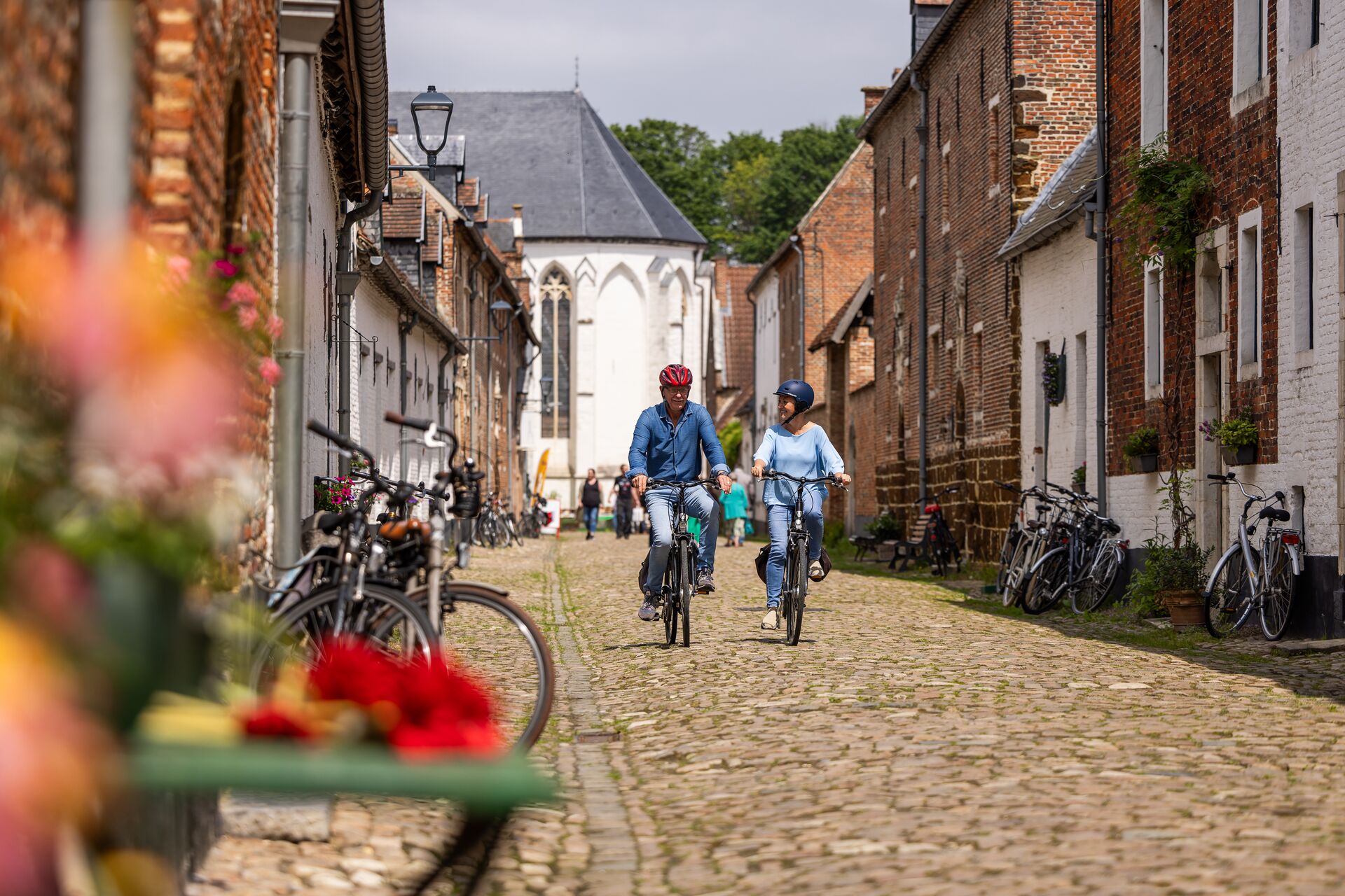Deze heuvelende fietsroute verkent de prachtige groene streek in het "Land van de Witte". Je fietst langs de Norbertijnenabdij in Averbode waar je in de schaduw van dit groots bouwwerk kan genieten van een ijsje in de welbekende "likdreef". Verder ontdek je via Zichem het bedevaartsoord Scherpenheuvel met zijn indrukwekkende basiliek. Geniet in Oranjestad Diest van een lokaal Gildenbier of Hagelands wijntje in het gezellig historisch stadscentrum. 2 fietsers rijden over kasseien langs de Norbertijnenabdij in het dorp Averbode.
