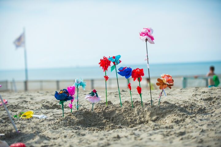 Colourful artificial flowers on sticks in the sand on the beach, with the sea in the background.