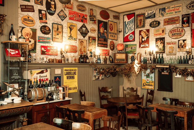Interior de un pub vintage y acogedor con mesas y sillas de madera. Las paredes están decoradas con coloridos carteles retro de cerveza y botellas, creando un ambiente nostálgico.