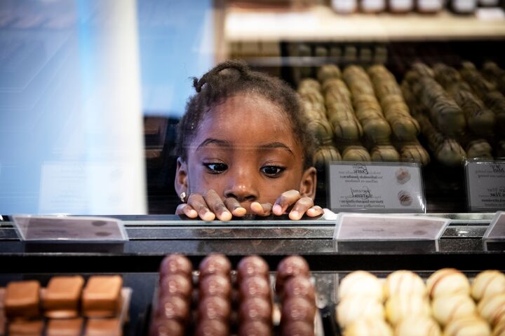 Un enfant observe avec curiosité une vitrine en verre remplie de différents chocolats, montrant son intérêt et son envie. L’arrière-plan présente des confiseries soigneusement disposées.