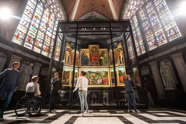 De Aanbidding van het Lam Gods in Gent: Een Meesterwerk dat Verwondering Opwekt Bezoekers bewonderen De Aanbidding van het Lam Gods, van de gebroeders Van Eyck, in de Sint-Baafskathedraal in Gent. De scène straalt ontzag en eerbied uit.