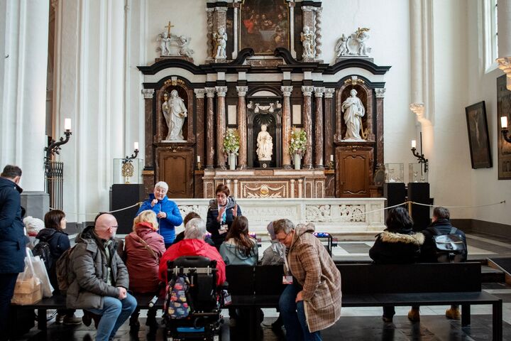Bezoekers in kerk met altaar Bezoekers zitten en praten op banken in een kerk met groot altaar en beelden op de achtergrond.