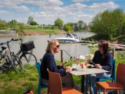 De Leie is onze leidraad op deze route. In Texture in Kortrijk duiken we in het verhaal over vlas en textiel. Sommige roterijen langs de Leie lijken in de tijd bevroren. Af en toe nemen we een omweg langs een oude Leiearm zoals in Bavikhove, Ooigem en Sint-Baafs-Vijve, prachtplekken voor een idyllische selfie. De Drietrapssluis in Ooigem is een sterk staaltje bouwkunde. Na de linkeroever te hebben verkend, steken we door naar de rechteroever. Zo passeren we de onthaalsite aan de Zavelput in Beveren – Leie. In het centrum van Harelbeke verlaten we de Leie. We dwarsen het provinciedomein De Gavers en volgen het jaagpad van het Kanaal Bossuit – Kortrijk terug naar de Guldensporenstad. Vlasleieroute_terrasje (c) Kris Jacobs