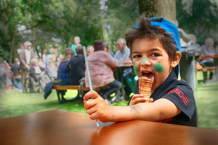 Un niño pequeño con una gorra azul está sentado en una mesa de picnic y disfruta de un helado.