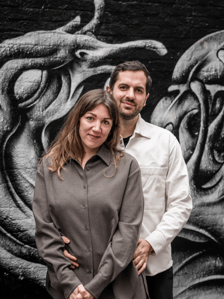 Ona Rombaut y Arne Breackman Hombre y mujer posan ante un mural en blanco y negro con figuras abstractas.