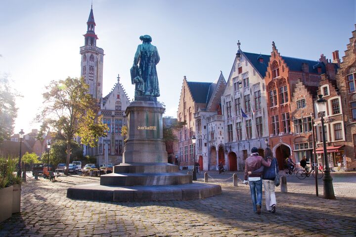 Piazza Jan van Eyck a Bruges. Le persone passeggiano per la piazza Jan van Eyck a Bruges. Nella piazza si può vedere una statua del maestro fiammingo Jan van Eyck.